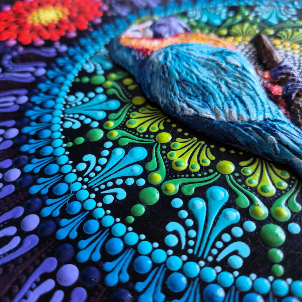 Detal rzeźbionej papugi i mandali dot painting na surowym plastrze drewna z korą.