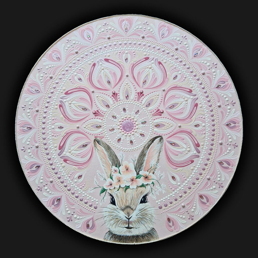 Obraz mandala w kolorze pudrowego różu z centralnie namalowanym zajączkiem w wianku z kwiatów. Technika dot painting.